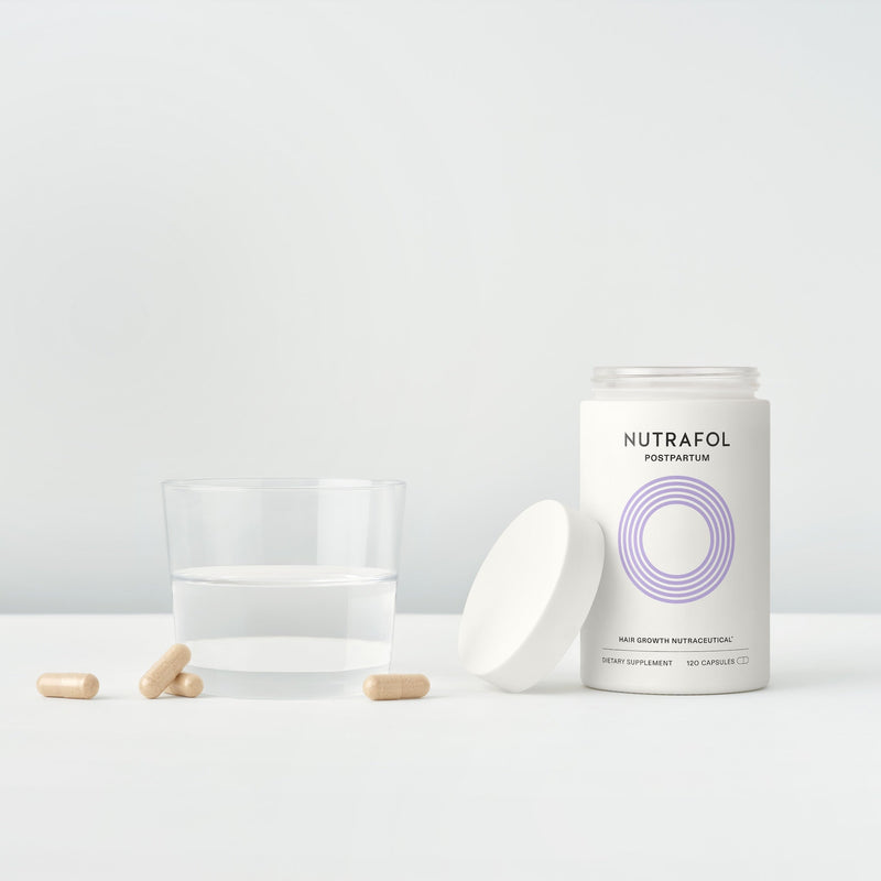 Nutrafol Postpartum hair growth nutraceutical with capsules in a neutral setting