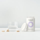 Nutrafol Postpartum hair growth nutraceutical with capsules in a neutral setting