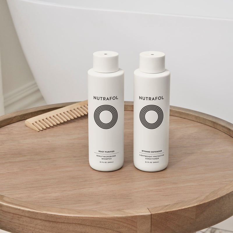 Nutrafol Root Purifier Shampoo and Strand Defender Conditioner displayed together beside a bathtub