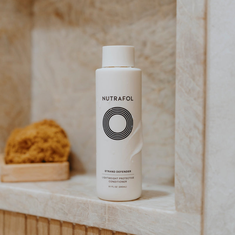 Nutrafol Strand Defender Conditioner displayed in a stone shower niche