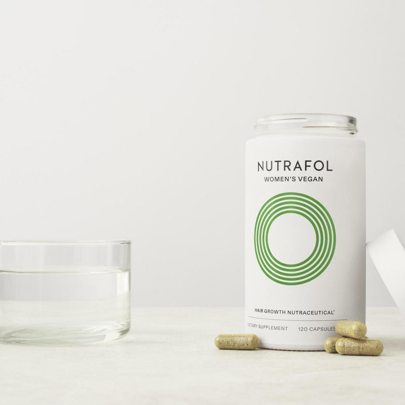 Open Nutrafol Women’s Vegan bottle with capsules and a glass of water