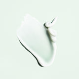 Glossy white cream texture of Oribe Curl Control Silkening Crème spread into a soft sweep with curled peaks on a pale green surface