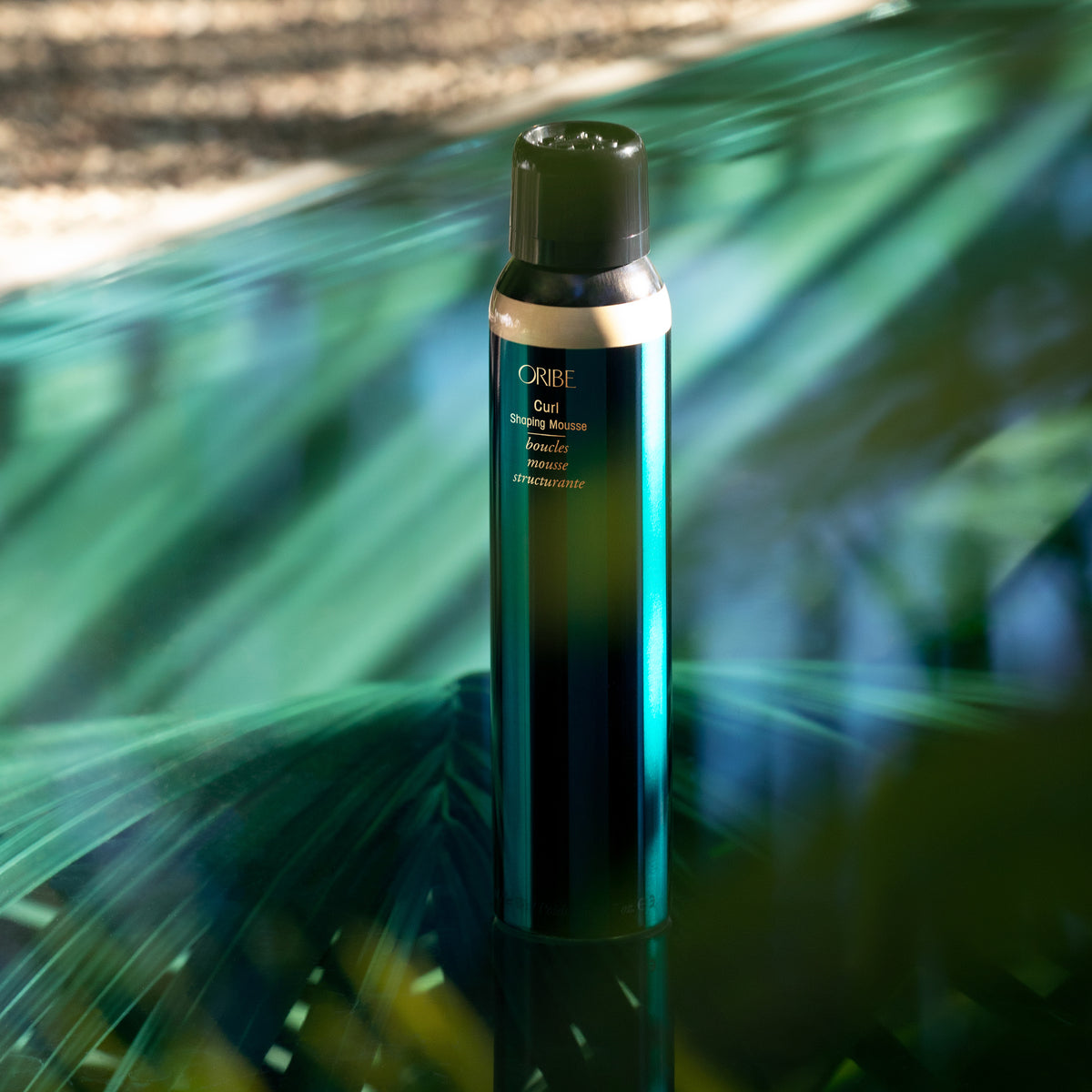Oribe Curl Shaping Mousse 5.7 oz bottle styled against layered emerald green fabric and natural shadow