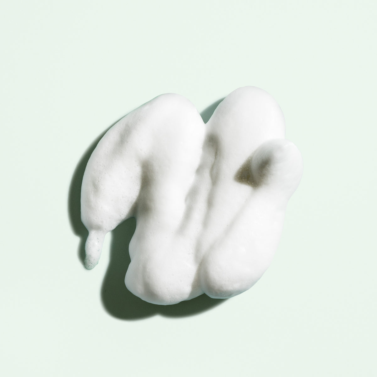 Airy white foam texture of Oribe Curl Shaping Mousse arranged on a pale green surface