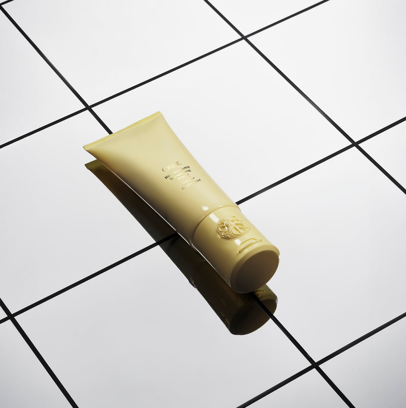Oribe Hair Alchemy Strengthening Masque tube on reflective white tiled surface.