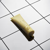 Oribe Hair Alchemy Strengthening Masque tube on reflective white tiled surface.
