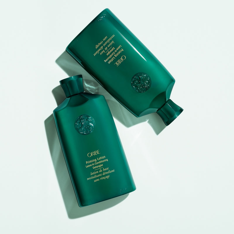 Two Oribe Priming Lotion Leave-In Conditioning Detangler bottles styled on a pale background