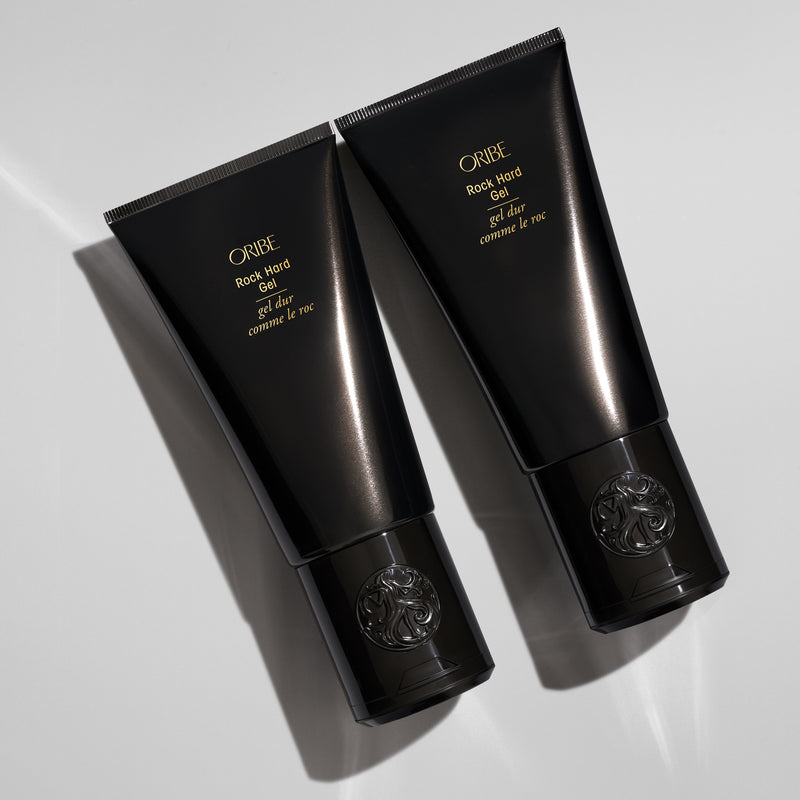 Two Oribe Rock Hard Gel black tubes arranged diagonally on a light gray studio surface with sharp directional shadows