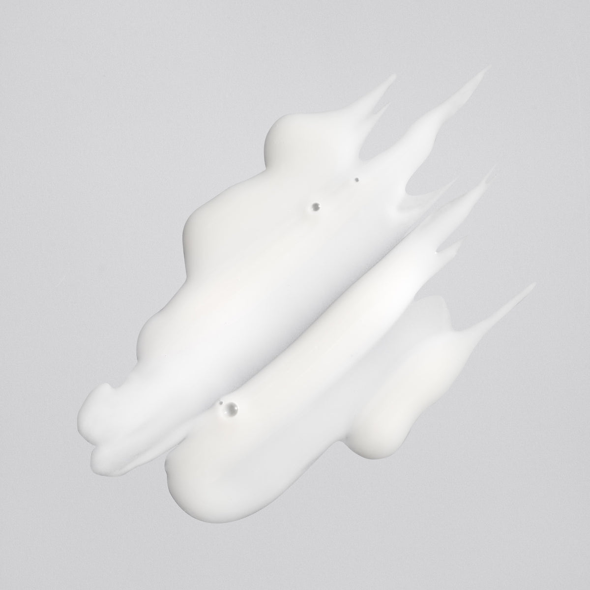 Creamy white texture of Oribe Rock Hard Gel spread into three sculpted strokes with pointed peaks on a pale gray surface