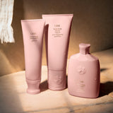 Oribe Serene Scalp Exfoliating Scrub arranged with Serene Scalp Balancing Shampoo and Balancing Conditioner on a pale pink studio background
