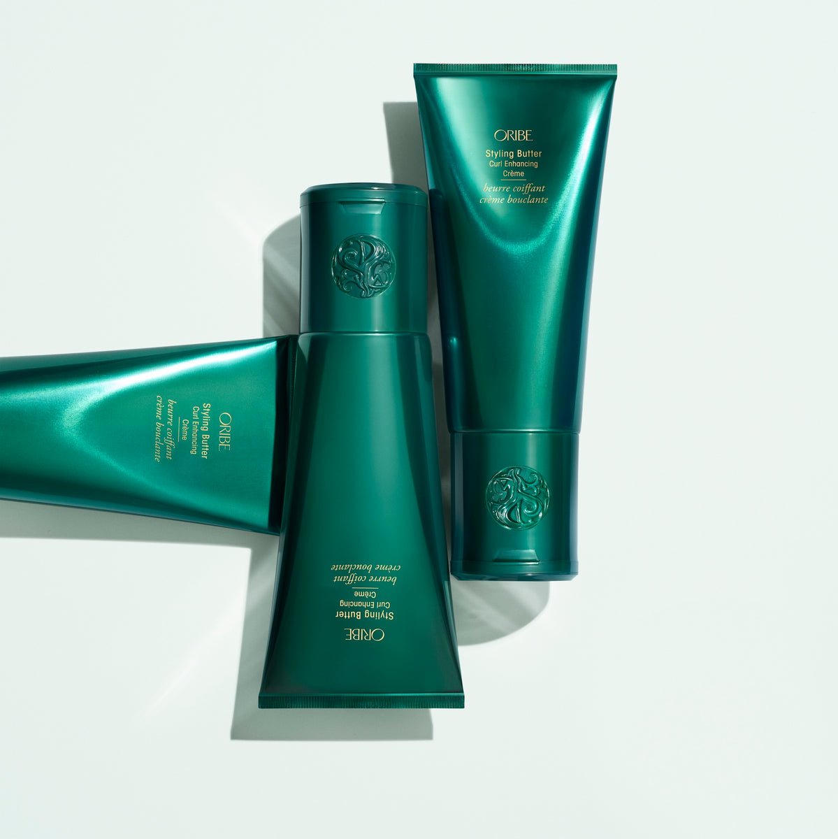 Three Oribe Styling Butter Curl Enhancing Crème tubes arranged on a white background